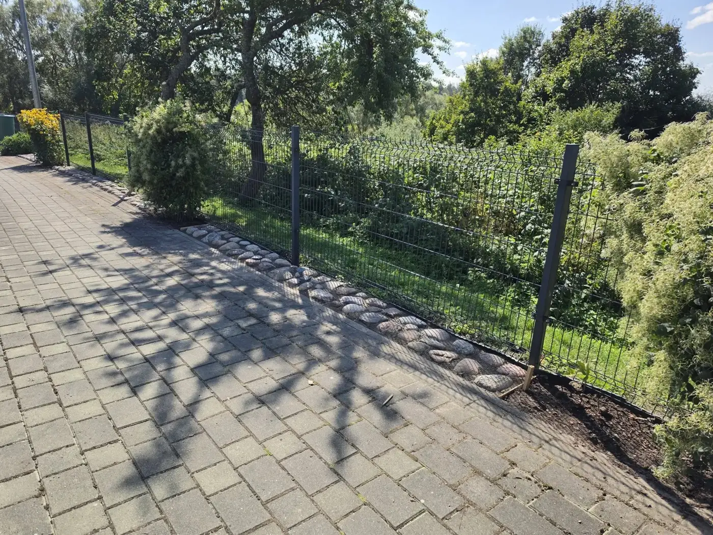 Trinkelių takas palei tvorą, saulėta diena