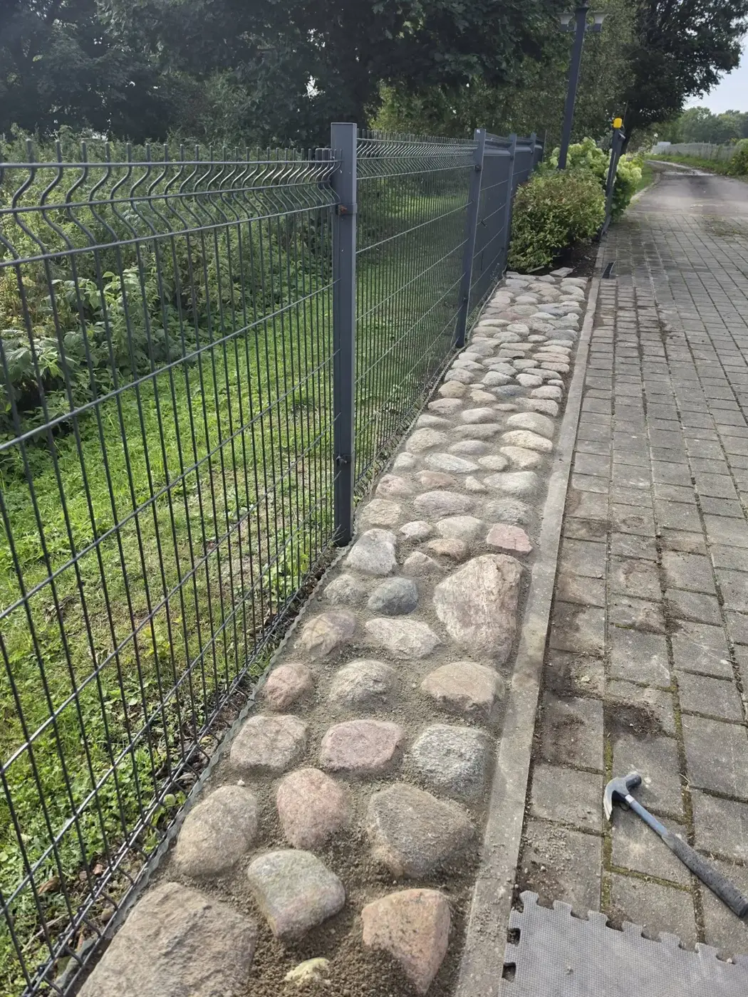 Baigta: akmenų juosta palei tvorą šalia trinkelių tako